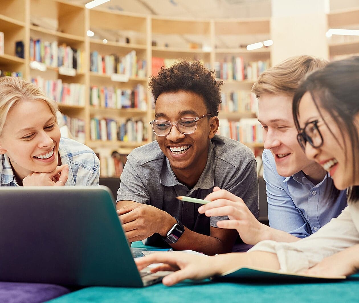University students collaborating around a laptop in a library